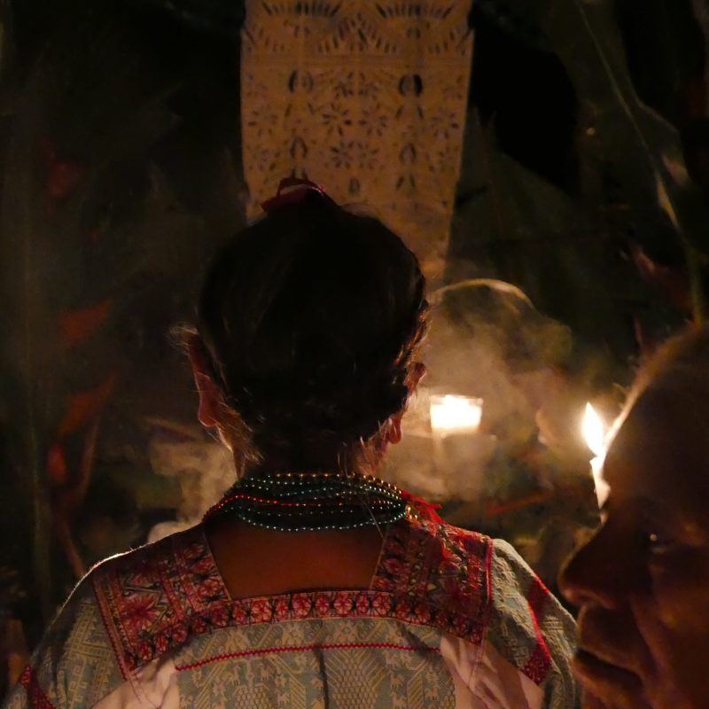 Mujer vestida con una blusa tradicional bordada frente al altar.